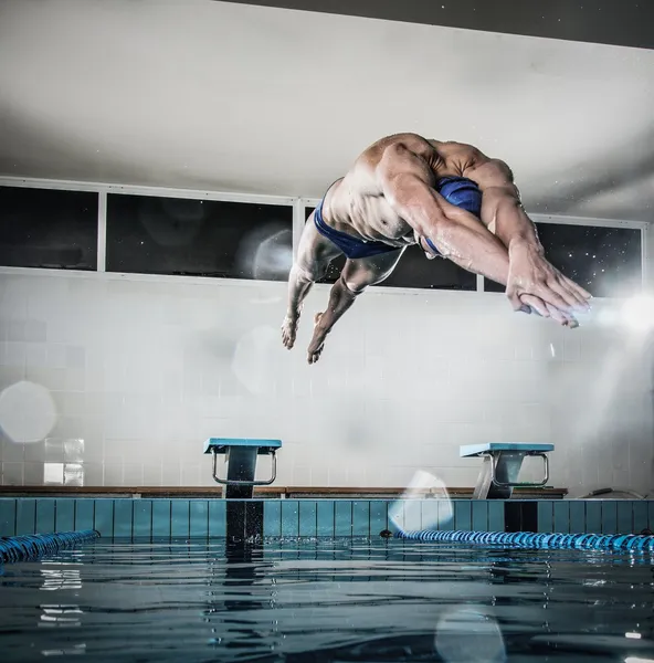 Молодые мускулистые пловец, прыгает от начала блока в плавательный бассейн — стоковое фото